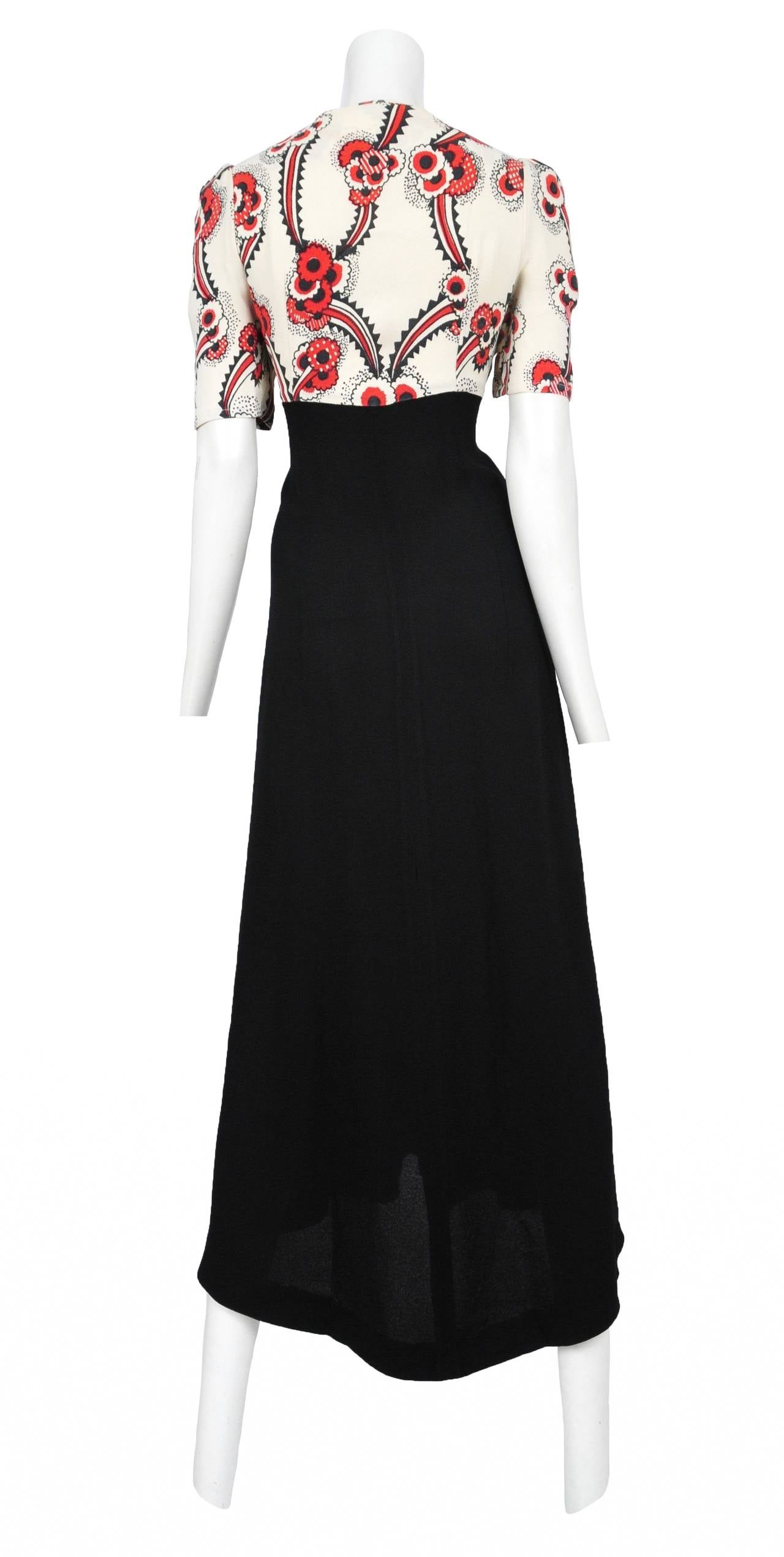 Vintage Ossie Clark moss crepe maxi dress featuring an iconic Celia Birtwell red, black and cream floral print on the short sleeve bodice. The bodice features a deep scoop neckline that is enclosed with a knot at the bust exposing a prominent