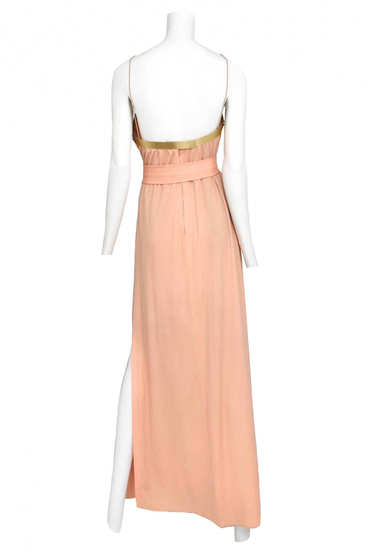 Vintage Jacques Cassia peach halter belted gown featuring architectural brass panels at the neckline, orange and brass detailing on the belt buckle and center chest panel, and gold chains adorning the bust of the dress. Circa 1970's.