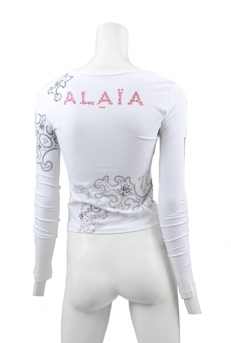 Bright white long sleeve cotton tee shirt with large red Alaia logo across back and black paisley print that swirls around arms & chest.