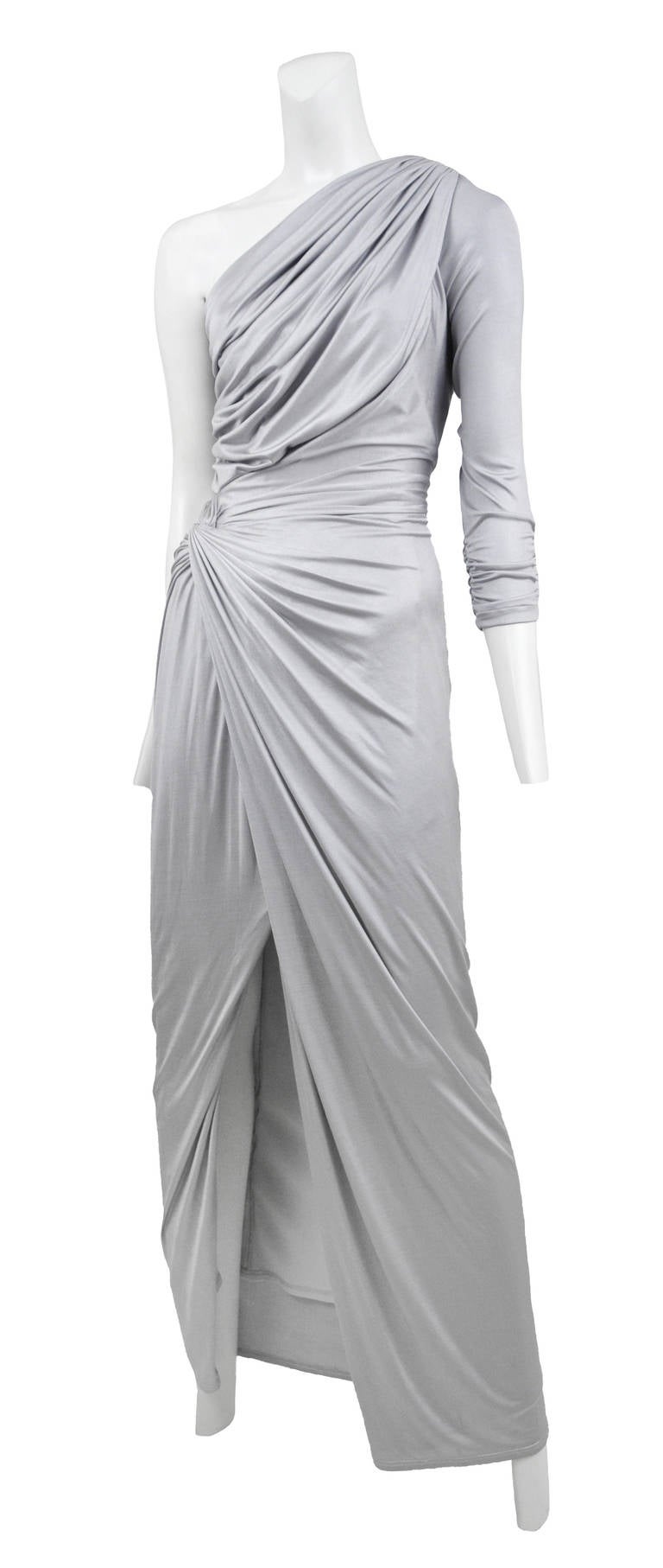 Metallic silver silk jersey asymmetrical  gown with ruches detail at waist and side zip closure. Front slit reaching to mid thigh.