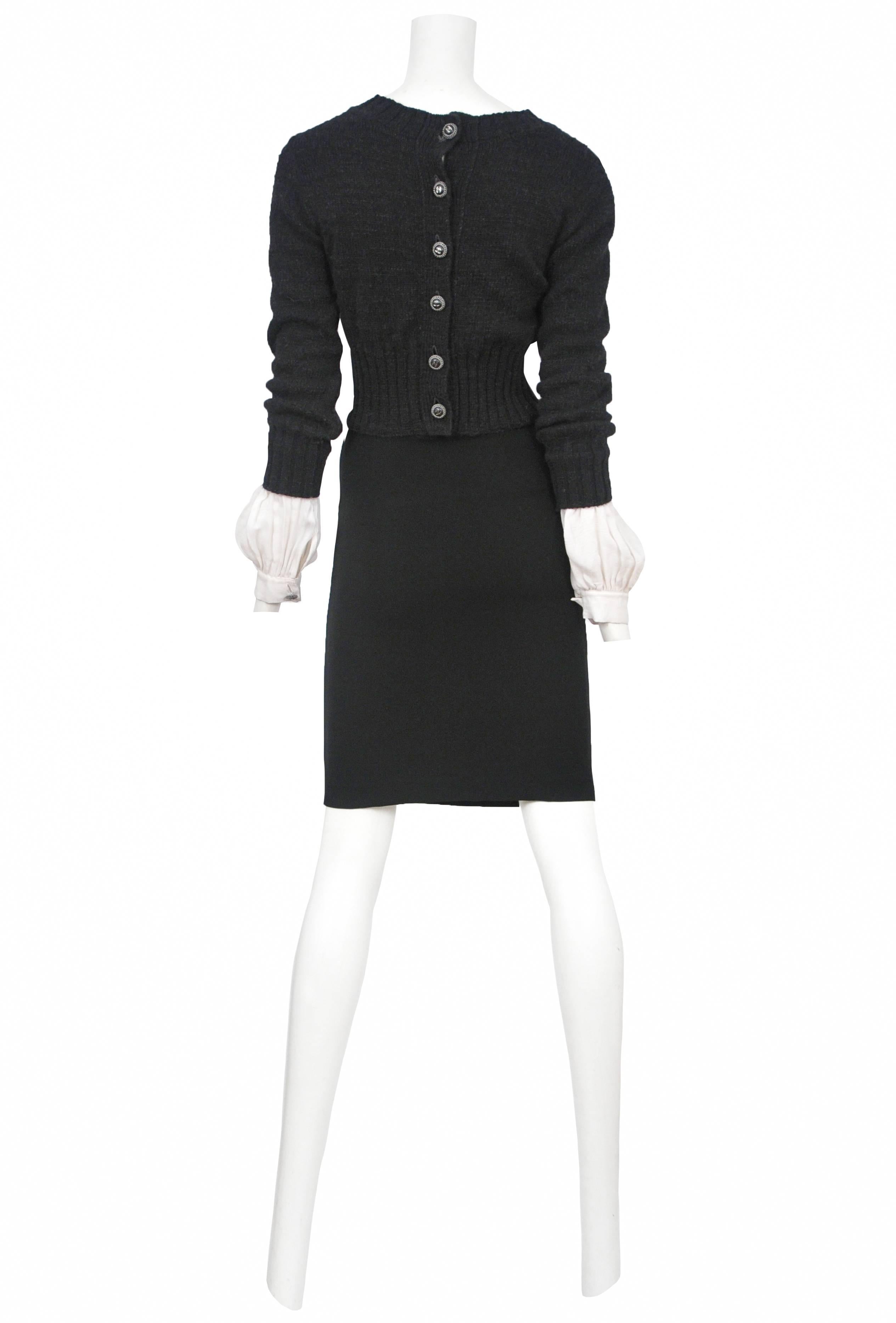 Vintage Chanel black sweater dress featuring a black crew neck sweater attached to a black knee length skirt, attached white shirt cuffs at the bottom of the sleeves, and a button back entrance.
