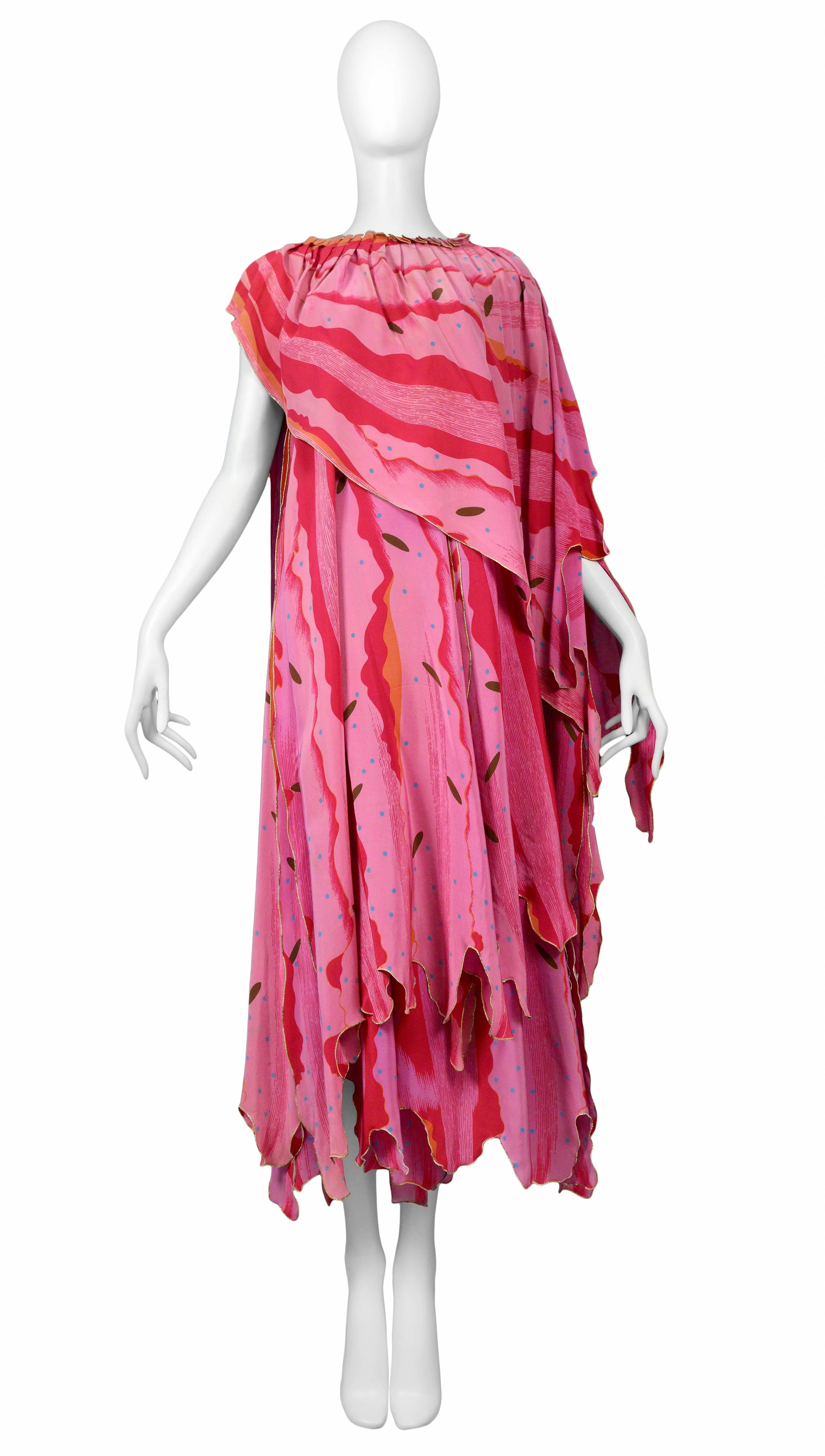 A rare and unusual Issey Miyake bright pink caftan ensemble featuring a layered pleated neck caftan and matching skirt. Both pieces feature an uneven gold marrow finish at the hem and an allover abstract pink print. Circa 1970's. 