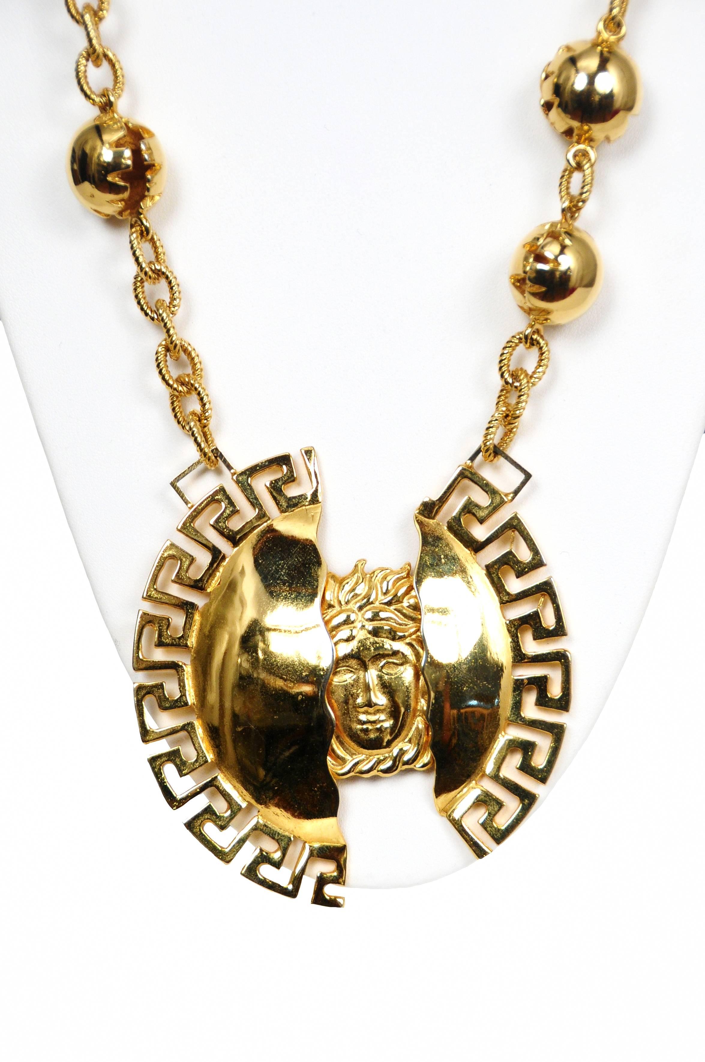 Vintage Versace gold tone necklace featuring a split fragment Medusa medallion that hangs from a gold tone chain interspersed with gold balls.