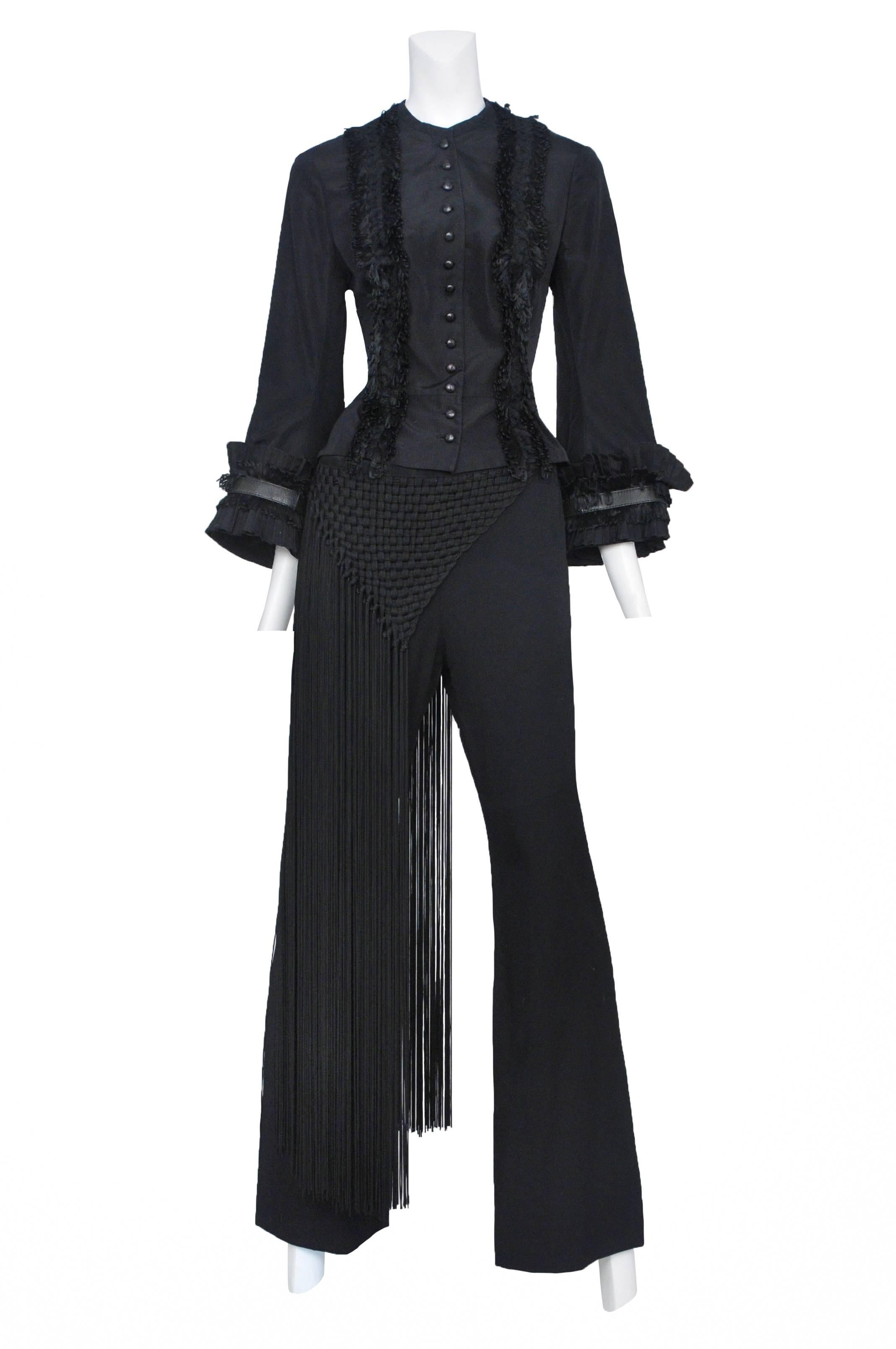 Fitted black taffeta jacket with ruffle trim, pleated sleeve trim and 13 front buttons. Black pants with woven cord detail at front and back with long fringe. Complete Look #49. Supercalifragilisticexpialidocious AW 2002. 