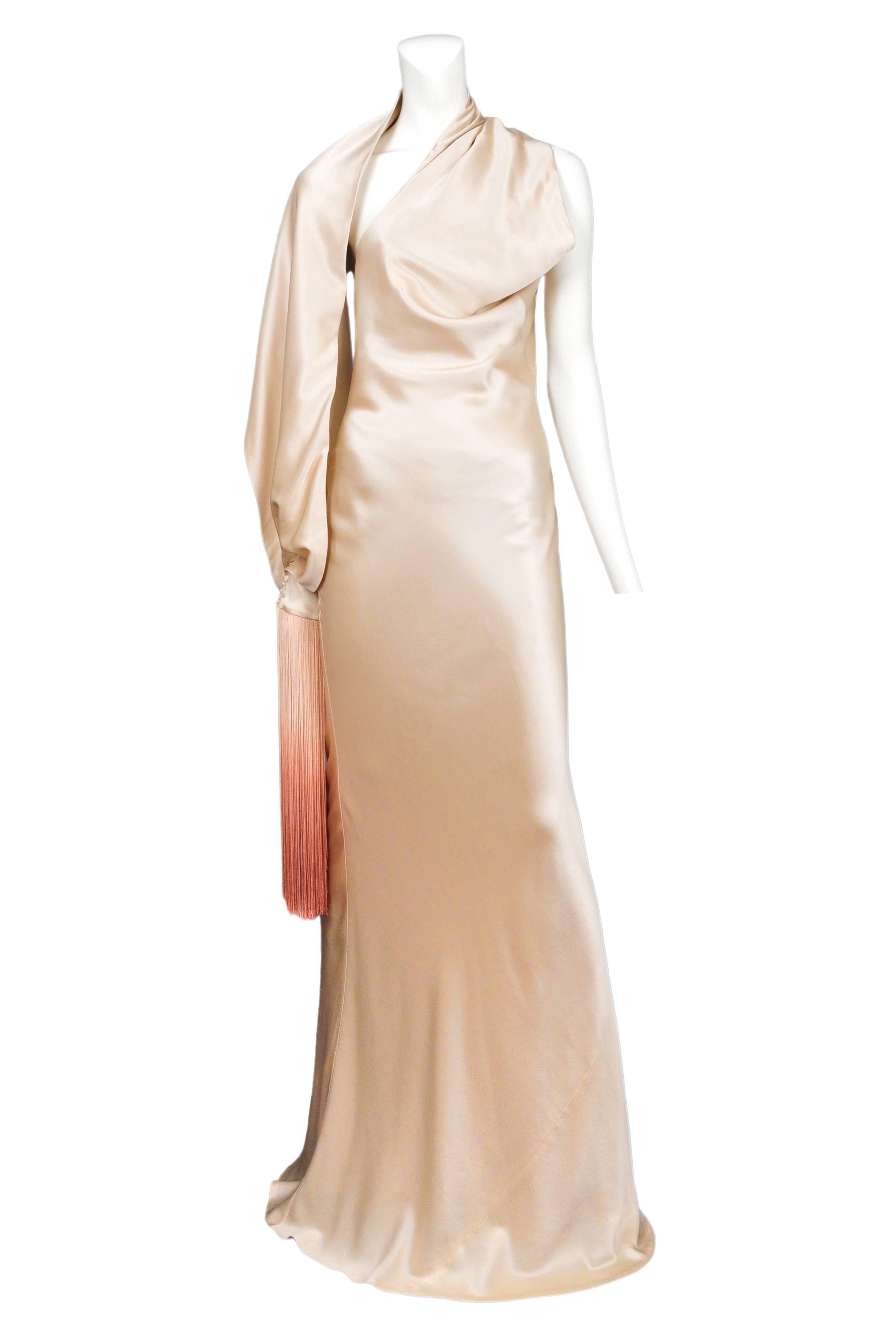 An off white satin asymmetrical bias cut gown with attached shawl sleeve with ombre fringe at cuff. Open back and covered buttons at side. Circa 2009. 

Please contact for more photos or information. 