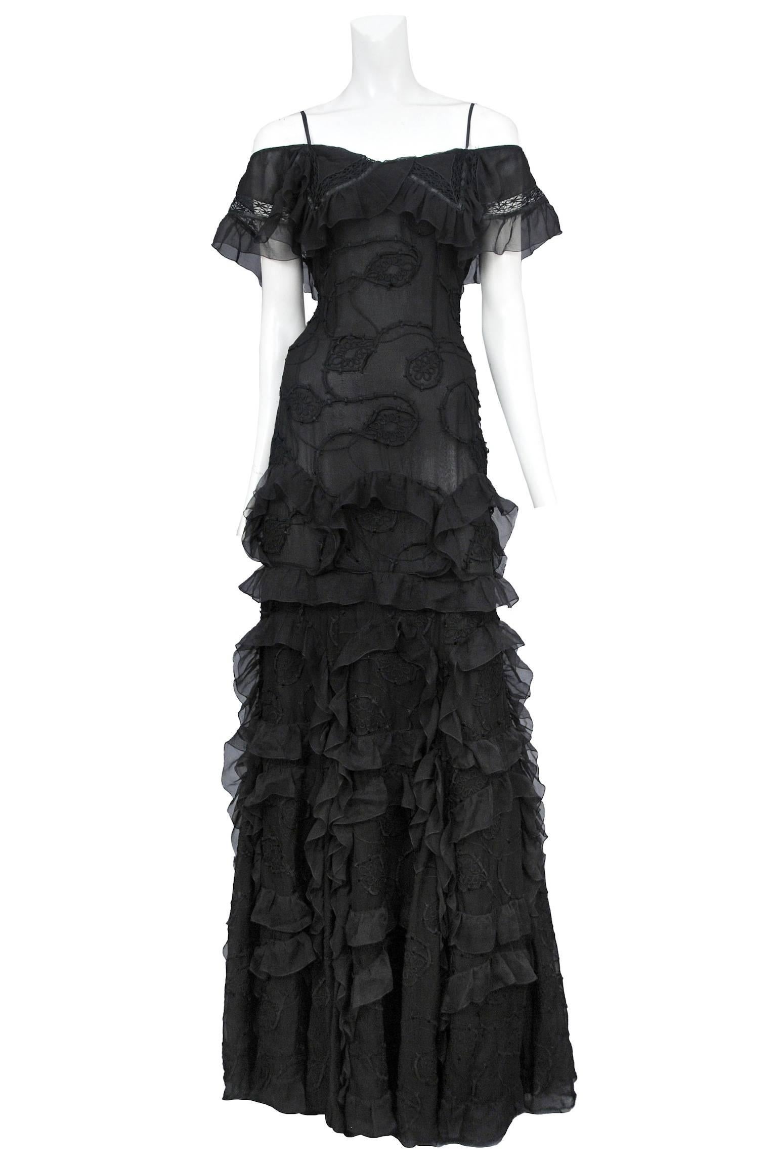 Vintage John Galliano black floor length gown featuring an off the shoulder neckline anchored by two spaghetti straps, tiers of curved ruffles adorn the skirt and black ribbon embroidery decorates the fitted torso and skirt.

Please contact us for