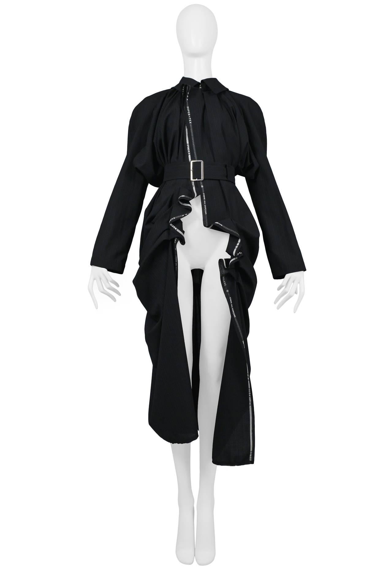 Comme des Garcons navy pinstripe coat features heavy draping, unattached belt, and exposed selvedge that reads "Comme des Garcons". Collection SS 2006.
