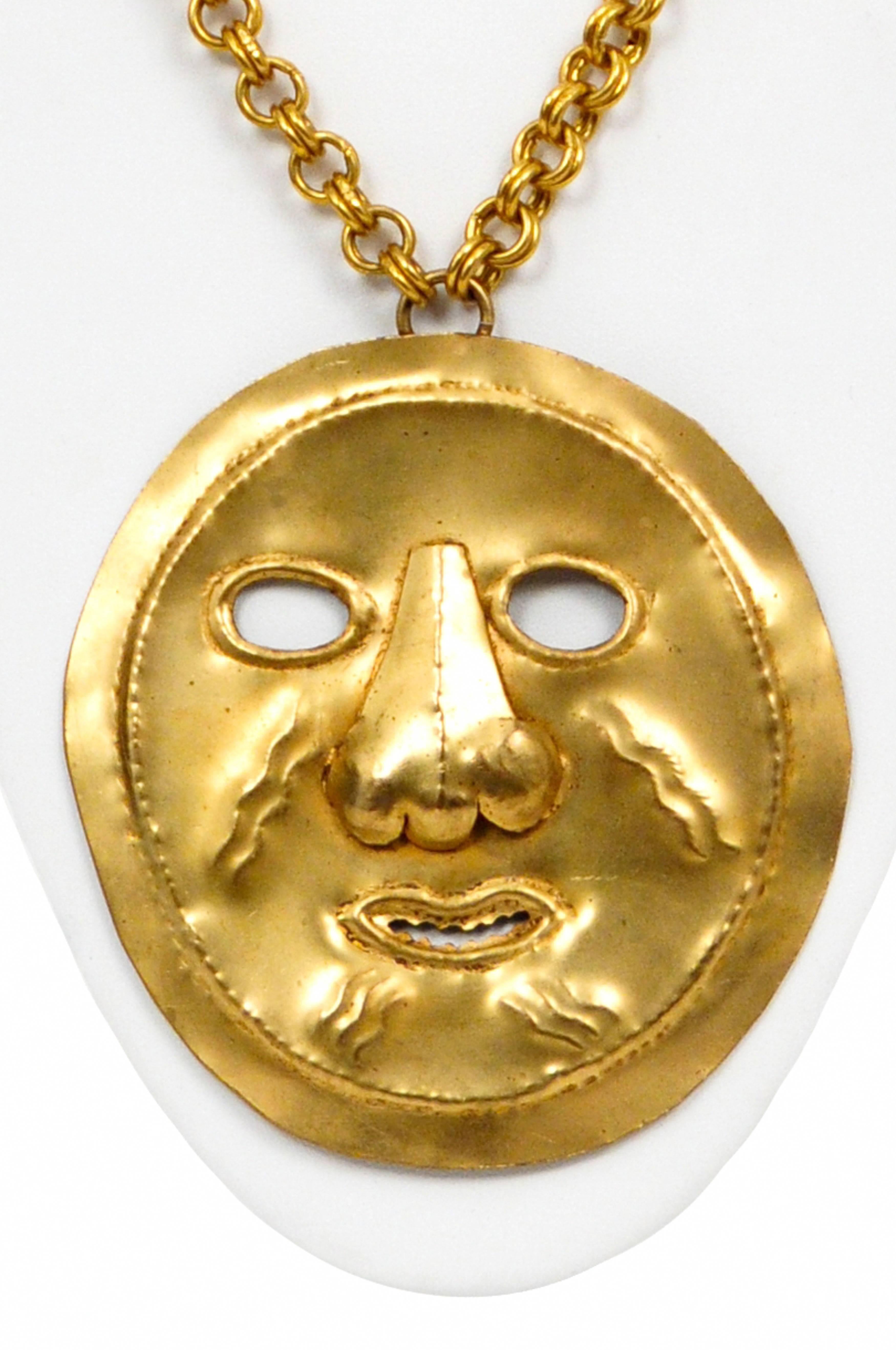 Vintage Yves Saint Laurent gold tone metal necklace featuring a large gold tone hammered metal mask pendant mirroring traditional Peruvian burial masks that hangs from a heavy gold tone chain. Extremely rare and the pendant appears to be hand
