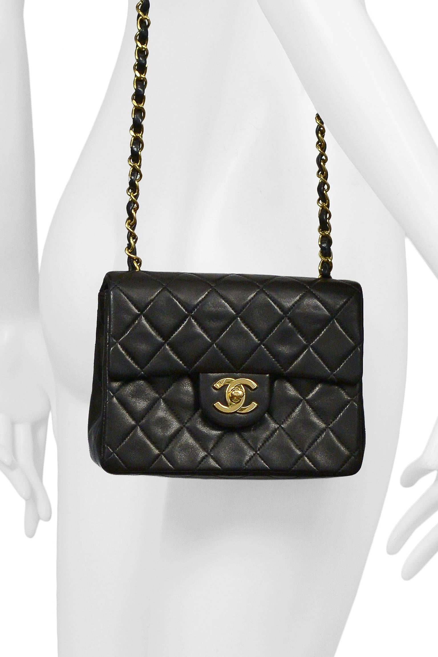 Vintage Chanel Classic mini bag in black quilted lambskin featuring leather interior lining, iconic leather and gold tone chain woven straps, a classic patch pocket at the back, one inner pocket, one inner hidden zip pocket, and a gold tone