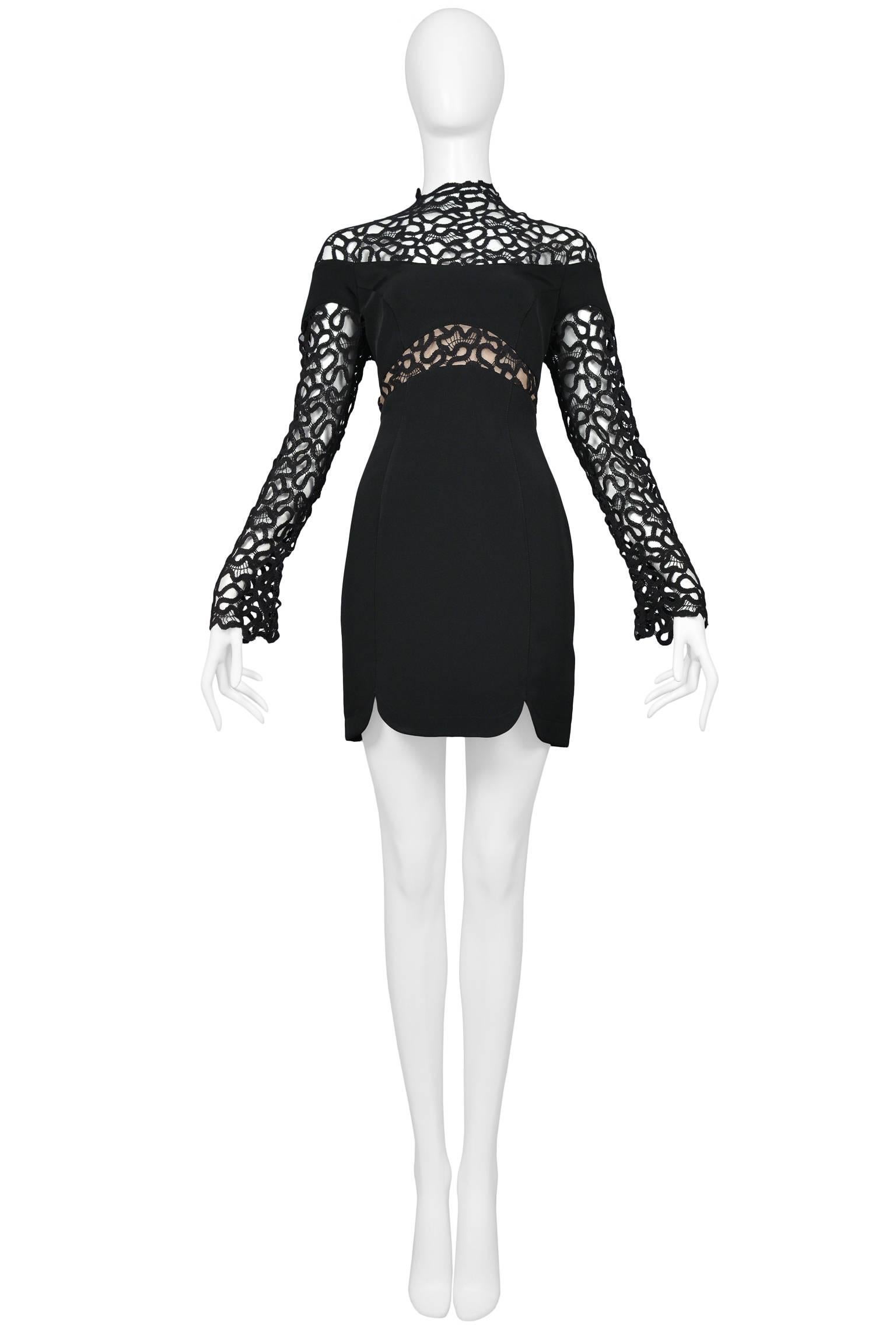 Thierry Mugler black squiggle lace and solid insets mini cocktail dress. The dress features a button up back, high neck, long sleeves, and a nude panel at center front. The skirt has two notches at front sides. Fitted body.