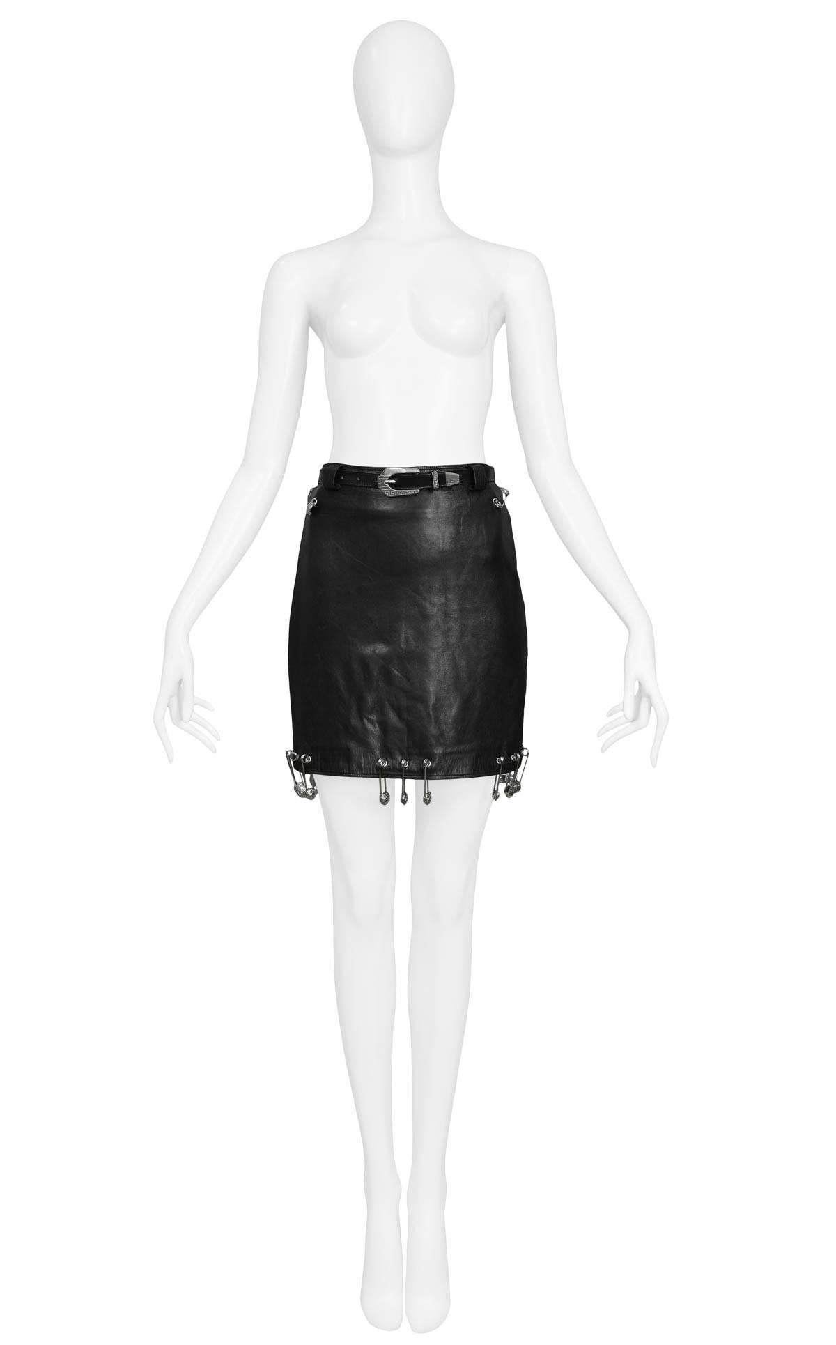 Iconic vintage Gianni Versace black leather skirt adorned with safety pins at hem & hips. Original silver-tone buckle belt with etched logo included with skirt. From the Spring/Summer 1994 Collection. 

