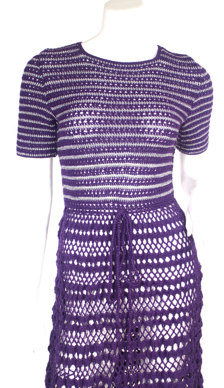 Early 1970's crochet knit dress. This dress is a lovely purple tone with accented silver knit crochet, silver buttons down the back, drawstring closure at waist.
