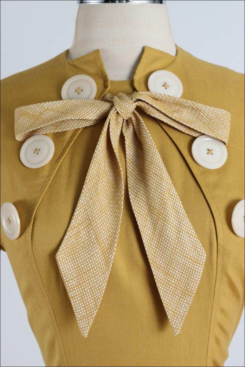➳ vintage 1940s dress

* mustard yellow cotton linen
* Ivory buttons
* large bow tie accent
* side pockets
* detachable matching shawl & belt
* metal back zipper
* by Paul Sachs

condition | excellent 

fits like xs/s

dress length
