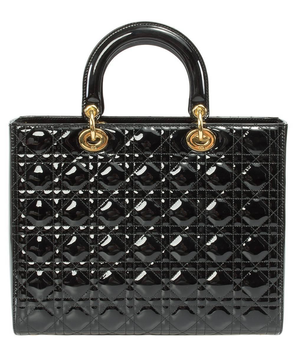 A definitive work of art, this black Lady Dior Bag in size large is meticulously handcrafted utilizing high quality sparkling patent leather from the legendary design house Christian Dior. The bag's timeless look consists of Dior's signature motif,