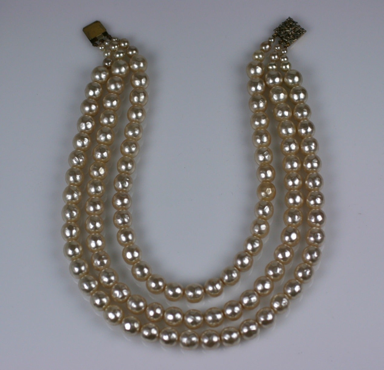 Elegant 3 strand glass pearl necklace by Louis Rousselet. Baroque and beautifully scaled cream graduated pearls which are handmade in the French tradition. Gilt filigree decorated clasp. Length 16