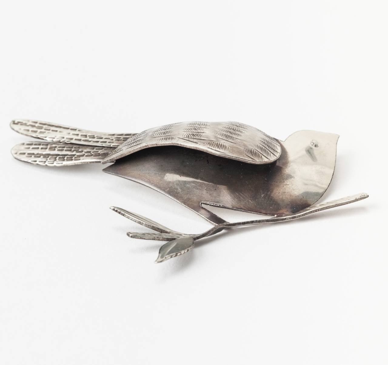 Spilla a forma di uccello modernista Rebajes Sterling realizzata da un unico foglio di metallo sterling. L'ala viene tagliata in un unico pezzo e ripiegata sul corpo, per poi essere ulteriormente decorata, così come la coda. L'uccello è appollaiato