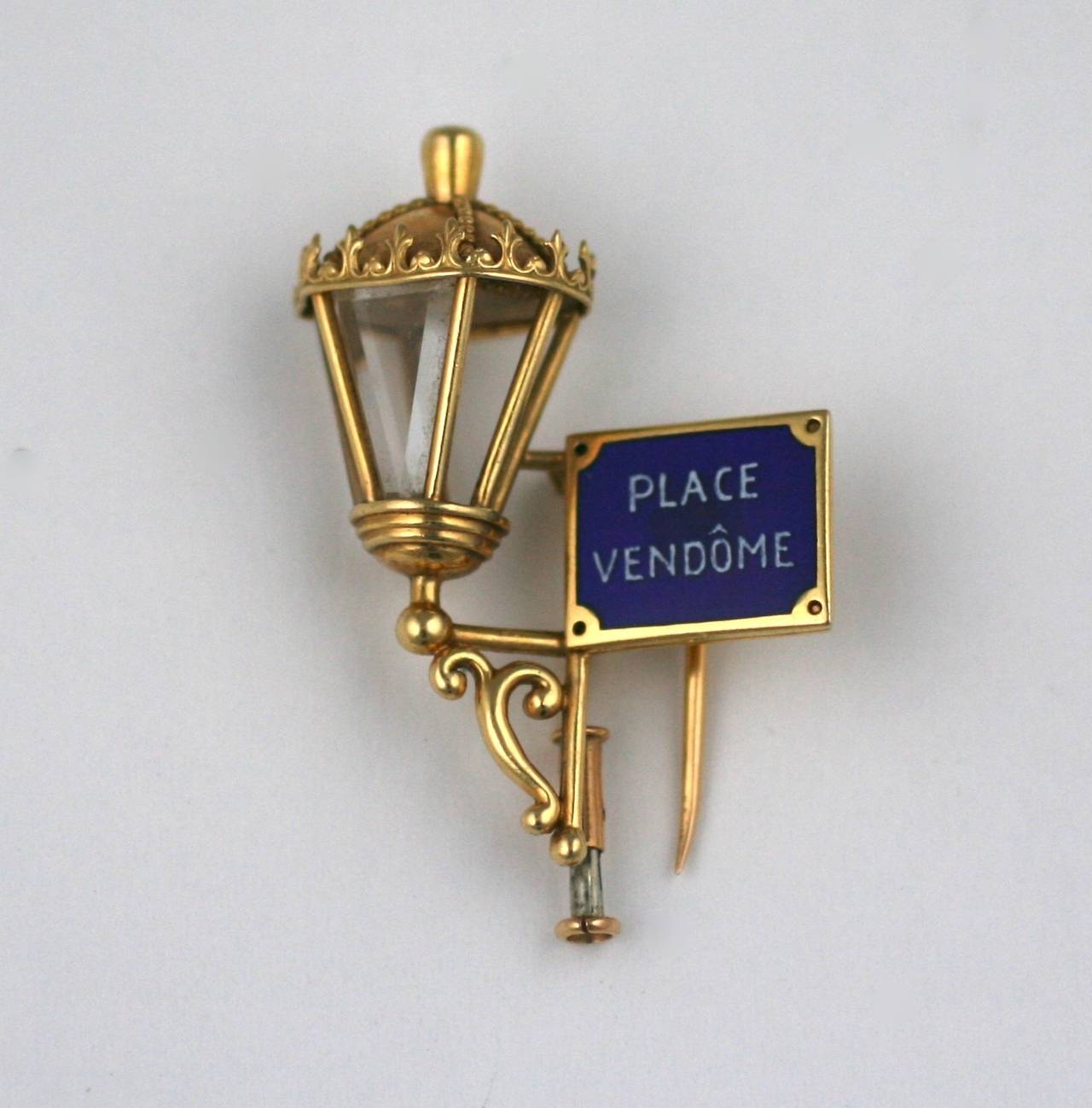 Mauboussin "Place Vendome" Lantern Clip in 18k gold. A charming (self promotional) fur clip from the 1940-50's with the address of the jeweler in blue enamel next to an antique street lantern rendered in 3D. 
There are glass panels across