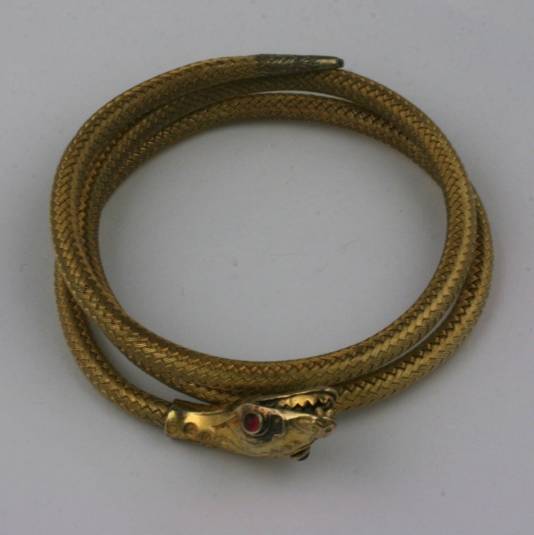 Victorian Coiled Serpent Bracelet from the late 19th Century. Details include ruby paste cabochon eyes with ferocious teeth and forked tongue. A steel coil within the woven wire band holds the bracelet tight against wrist. 1880's.
Excellent