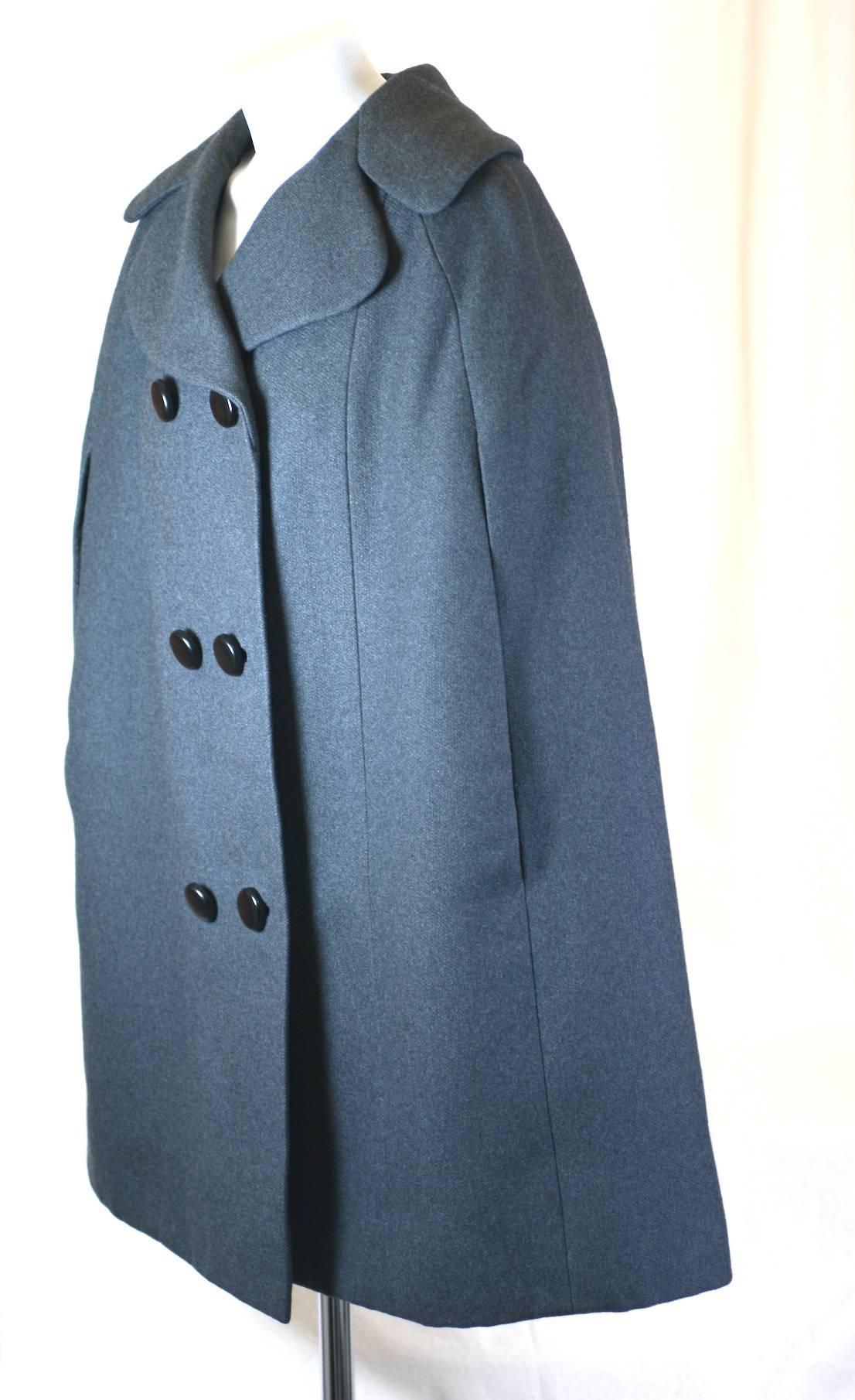 Norman Norell Gray Wool Flannel Cape with 2 arm slits. Bell shaped with large cutaway notched collar and double breasted closure. 
Immaculately tailored by Norell with black silk taffeta lining. Worn with arms inside, this cape becomes