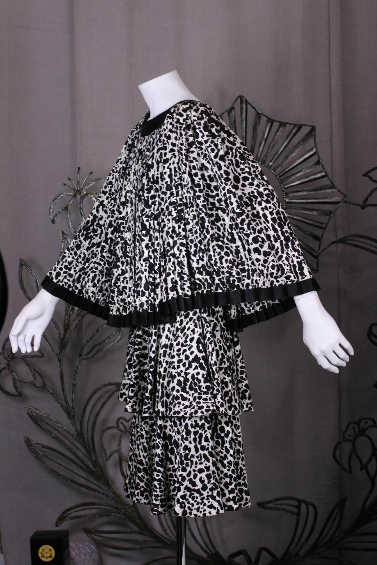 Unusual Galanos Knife Pleated Tiered Silk Crepe Dress. A sleeveless sheath dress in same abstract black/white animal print silk forms base of dress with a tiered flounce at hip and mid thigh.
A knife pleated full capelet (attached) falls from the