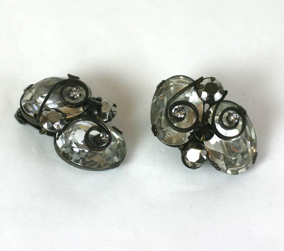 Striking Schreiner crystal ear clips with hematite and jet stone accents. Stones are set into japanned metal which provides a striking contrast. Scrolled metal accents are overlaid like French iron work. These clip earrings are unsigned. 1950's USA.