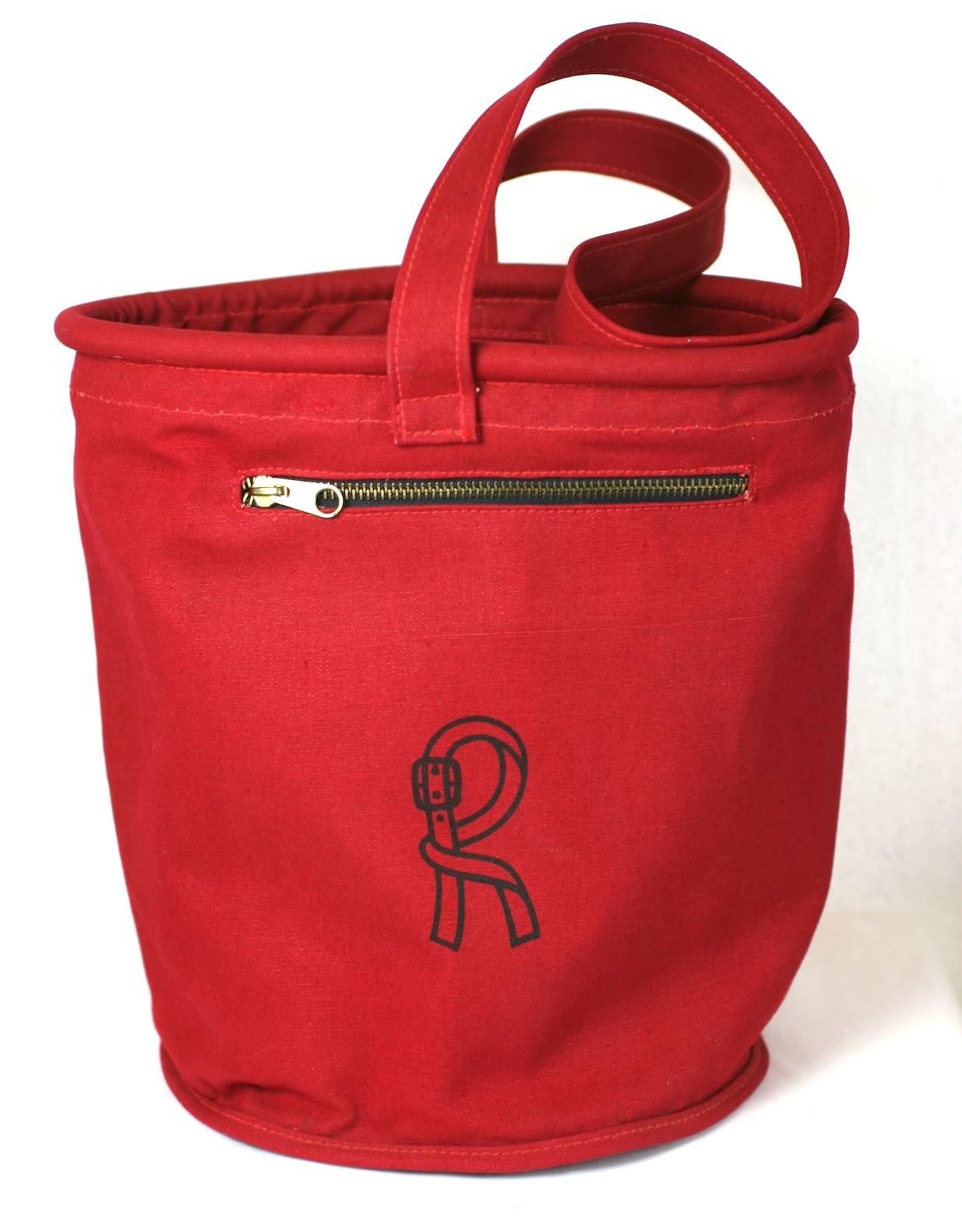 Sac à dos rouge Roberta di Camerino des années 1970. Sac seau en toile rouge avec des poches zippées en quinconce qui font le tour du sac. 
Logo imprimé en bleu marine sur le devant et tubulure raidie sur le bord supérieur. Italie, années