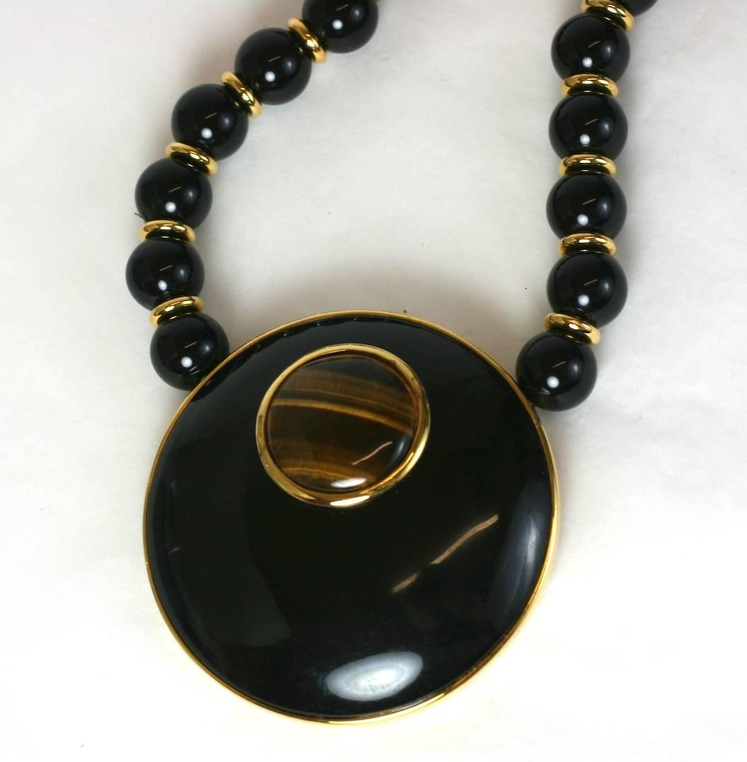 Alexis Kirk Statement Necklace in Black resin with genuine tiger eye cabochons.
Large circular pendant is embedded with an off center tiger eye stone. The hidden hook clasp is also decorated with a similar stone.
Very striking without the weight of