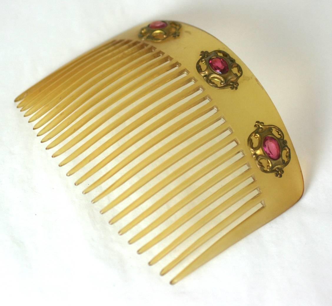 Blond celluloid (replicating Horn) Art Nouveau Comb with 3 gilt filigree applications and rose paste stones from the turn of the 20th Century. Simple form with a lovely pop of color. 1900 France. 
5