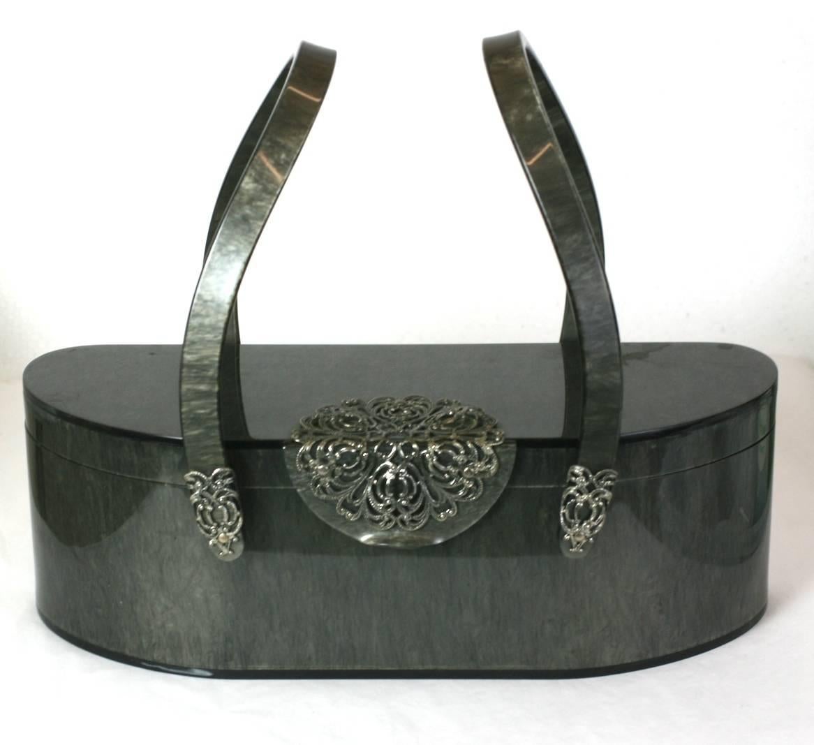 Marbleized Gray Bakelite Purse from the 1950's. Unusual shape with curved handles decorated with silvered filigree accents. Interior mirror within lid. 1950's USA. 

11" x 3.5" x 3.75"high. Handle 8" in height. 