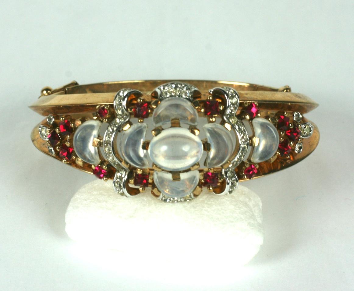 Trifari Alfred Philippe, Clair de Lune collectible and elegant hinged bangle bracelet of gold plated metal, crystal rhinestones and faux demilune cut moonstones and rubies. 
Marked: Trifari with Crown, 1950's USA. 
Excellent Condition. Width 1