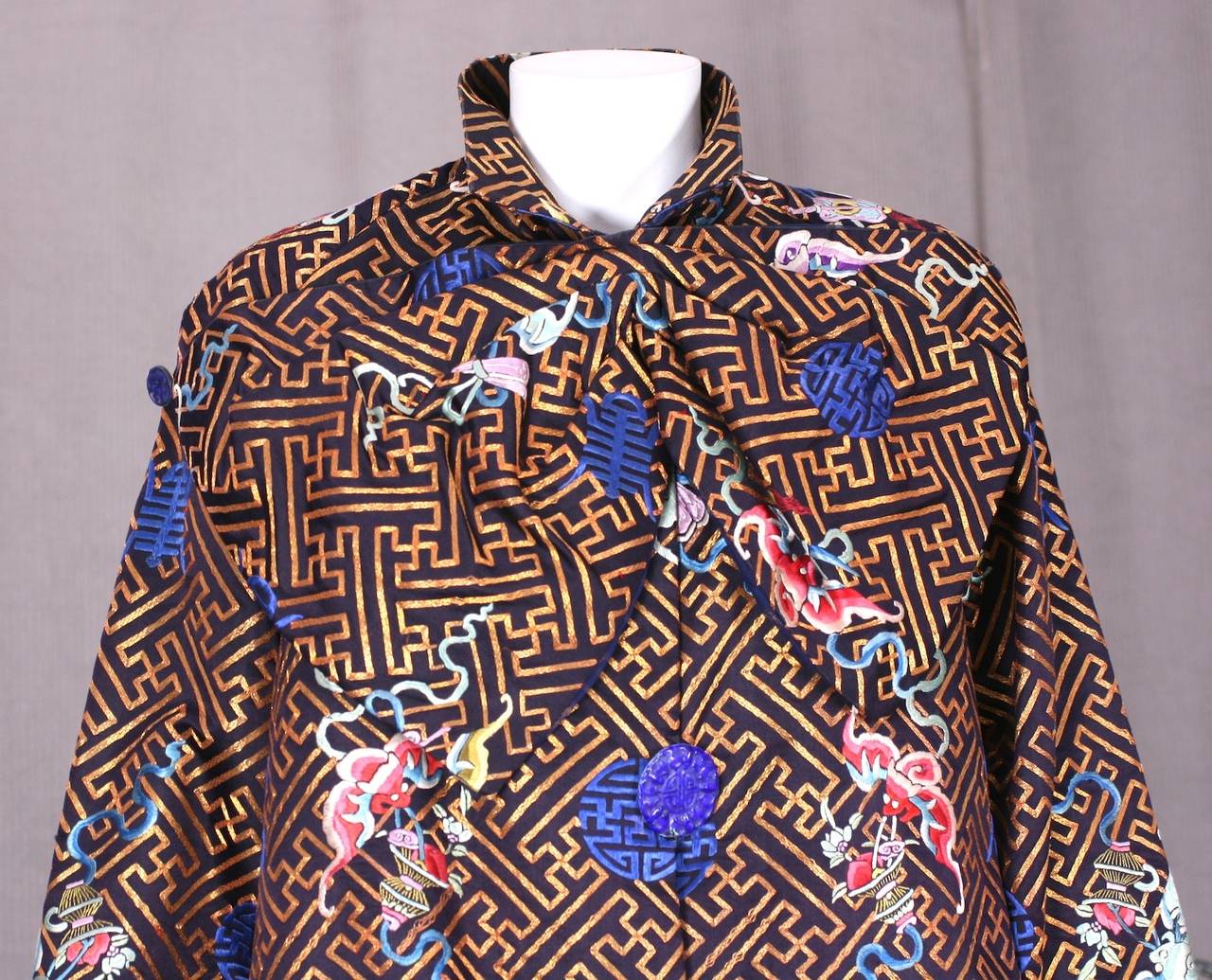 Art Deco coat from the 1930's retailed in Peking (Beijing), China. A lavish antique Chinese textile is used to construct the coat with an easy, wearable cut.
There are 2 large blue enameled buttons on the center front and a large gathered bow is