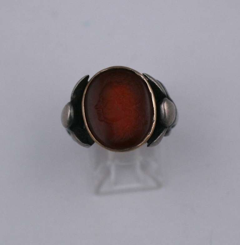 Antique Carnelian Intaglio Ring from the mid to late 19th Century. Intricately and finely carved seal of a Louis VIII profile within a gold bezel and an Arts and Crafts sterling silver ring setting with abstract fairies mounted on the shoulders.
