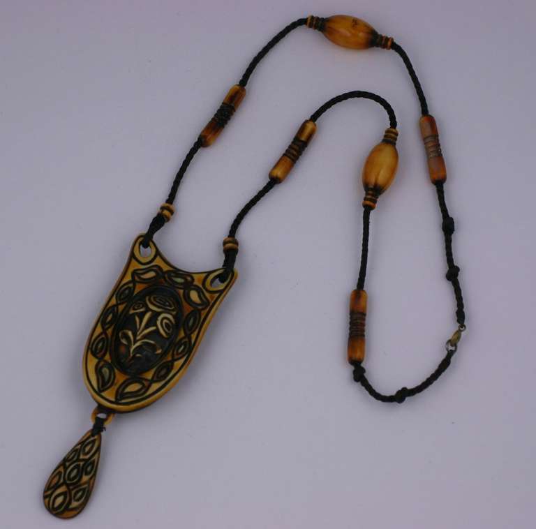 Insolita collana da flapper in celluloide patinata degli anni '20. Il ciondolo a forma di bombe è inciso e decorato con un motivo floreale. Le perline abbinate sono distribuite lungo il cordone di seta. 24