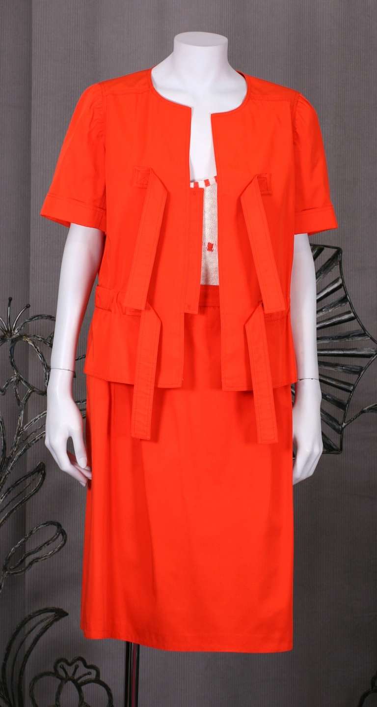 Bright orange cotton twill ensemble by Andre Courreges, Paris. Jacket has hidden hooks under a center front placket which closes with 4 self ties. The jacket has a gathered belt inset in waist. Skirt is slightly A line with gathered waist. There is