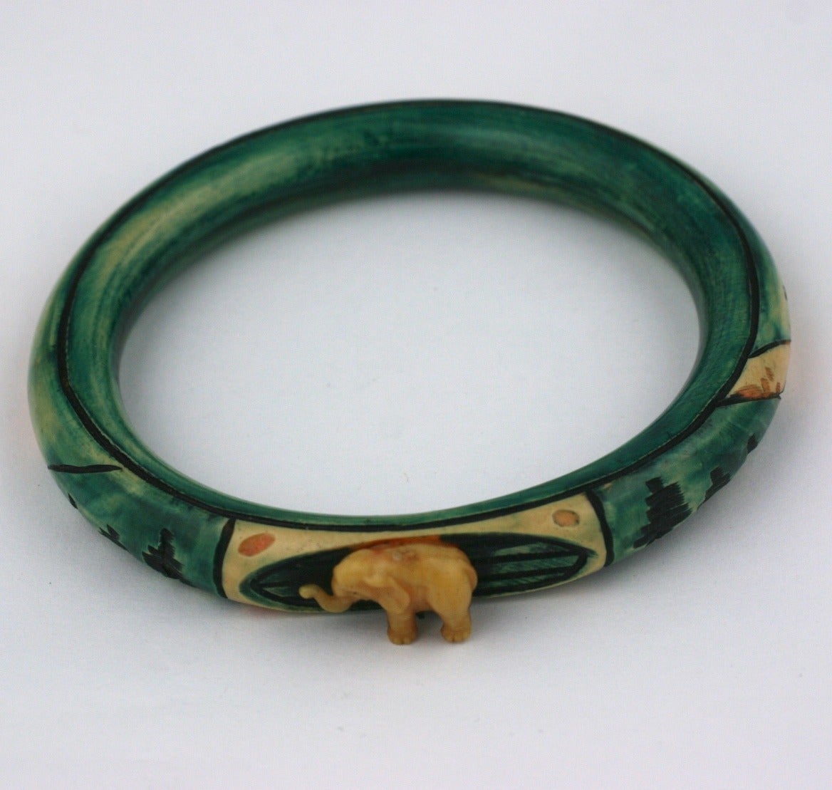 French Art Deco Anglo Indian celluloid carved, painted ,and stained bangle bracelet. The top motif centers a three dimensional lucky (trunk up) elephant.The body of the bracelet is carved with various flora and landscape in deep emerald, cream and