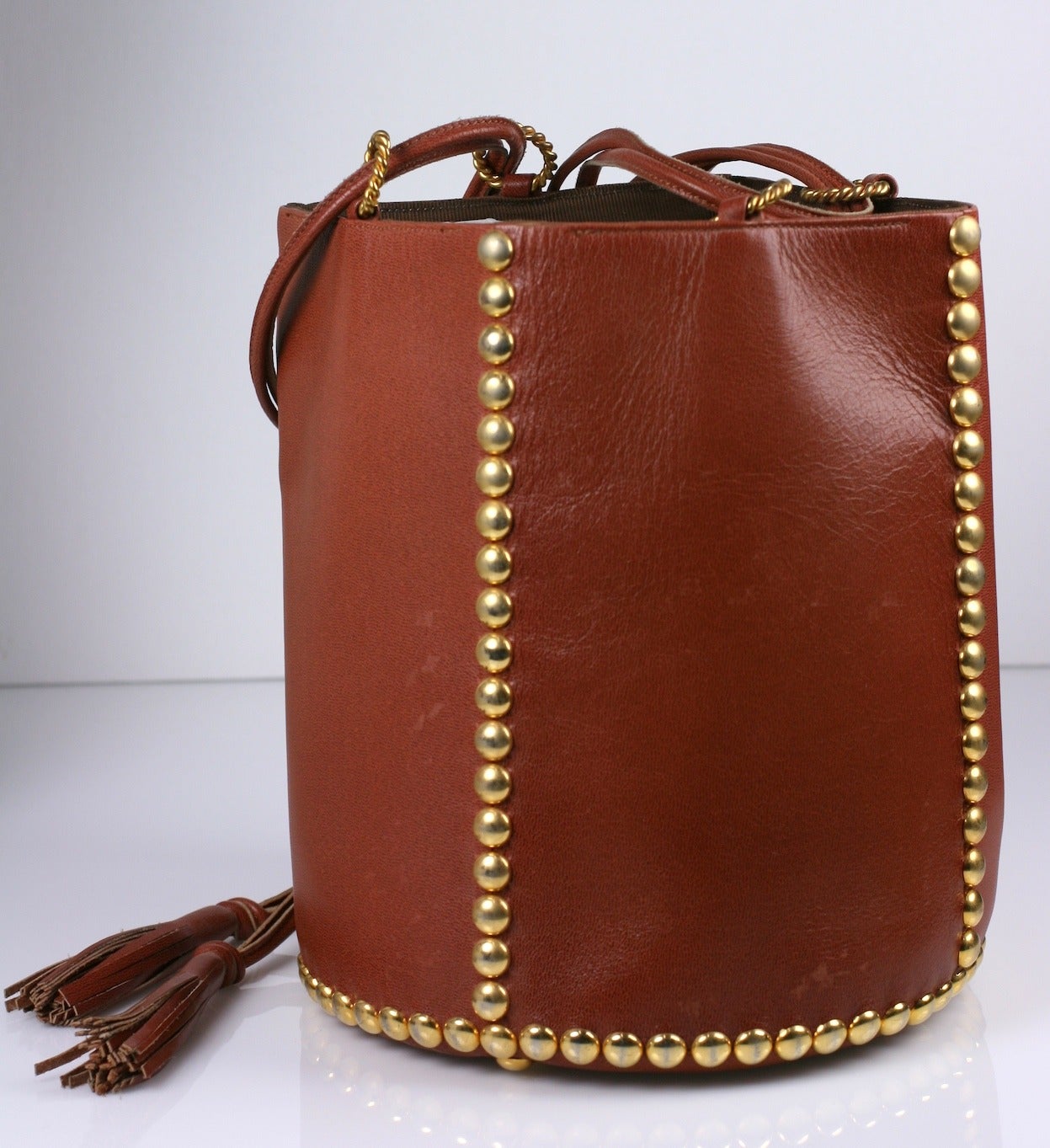 Renaud Pelligrino Studded Bucket Bag in deep caramel leather with round gold studs in 4 lines running down the sides. Leather drawstring with tassel allows bag to work as shoulder or hand held. Lined in faille. 7