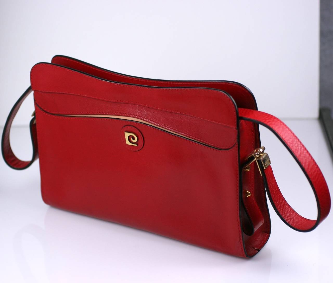 Pierre Cardin red leather shoulder bag with gilded PC logo. One exterior pocket with zippered central compartment. Interesting metal fittings on shoulder strap (non adjustable). Excellent condition. 1980's France. 
10.5