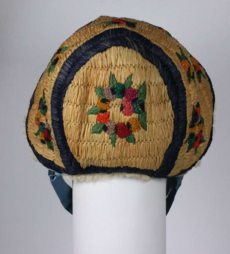 Poiret directoire style raffia cap with Martine style floral wreath embroideries. Although perceived of as a night bonnet, these were usually worn with late afternoon empire styled dresses. Cap is in excellent condition, lined in blue silk. 
The