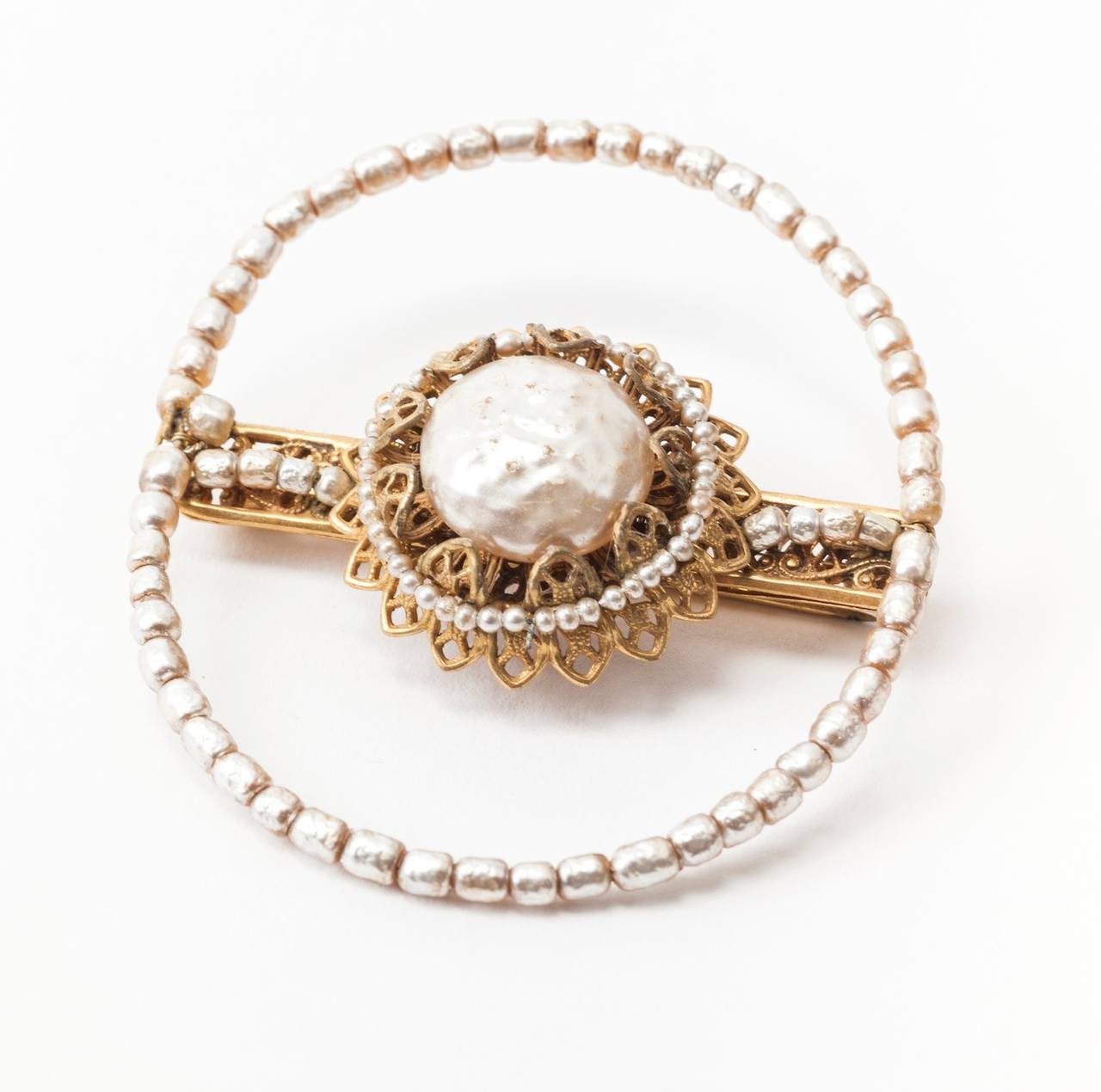 Miriam Haskell brooch with signature large baroque faux pearl and small baroque pearls wired to form a bar pin. An additional wired pearl surround encircles the brooch. The faux baroque pearls are set in signature Russian Gilt filigree. 1950's USA.