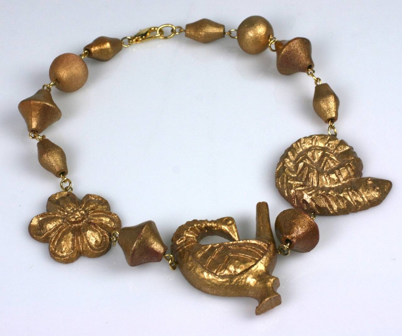 Kenzo carved and gilt wood composition figural necklace. Composed of a backward glancing goose, coiled serpent, and classical floral rosette and strung with lantern and round gilt beads. Excellent condition.
Length 17