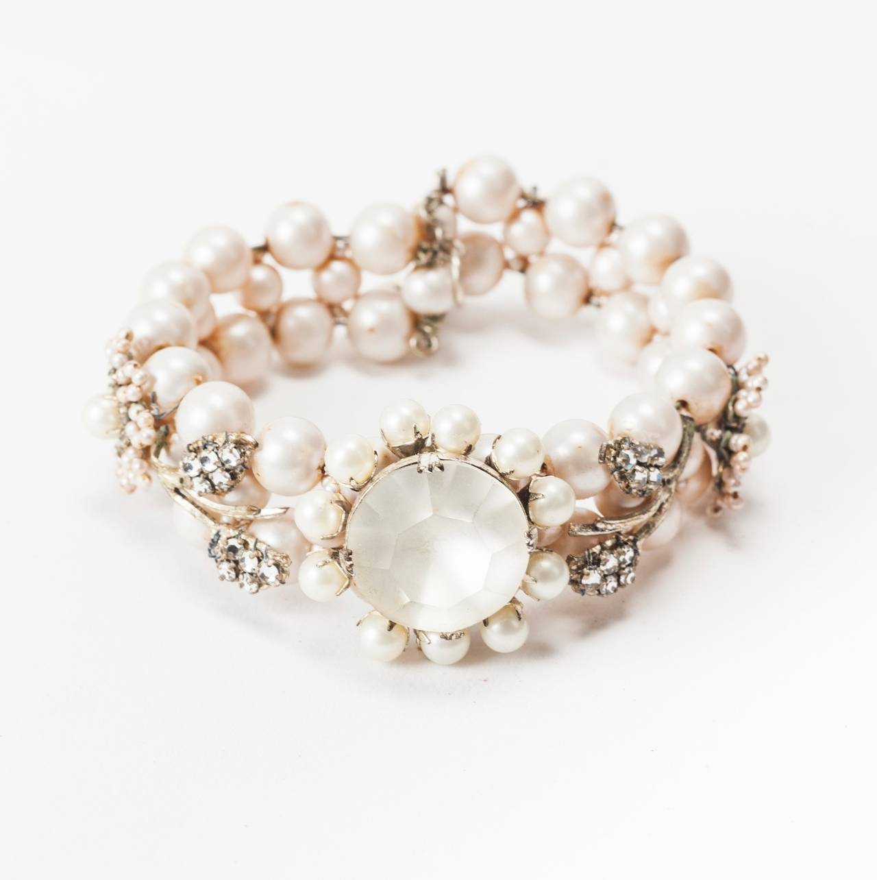Miriam Haskell signature round freshwater faux pearl flexible cuff bracelet. 
The center motif has a frosted cut crystal flower head surrounded by gilt set round pearls.The bracelet body is decorated with hand sewn crystal rose monte flower and