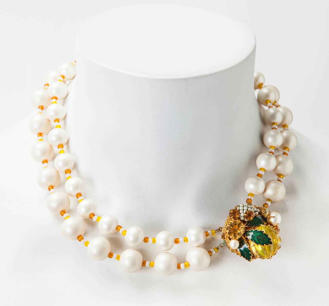 Miriam Haskell's Signature freshwater faux pearl double strand necklace.The two varying size strands are spaced with topaz and white pate de verre seed beads.The elaborate clasp is embellished with emerald green enamel leaves, faceted prong set