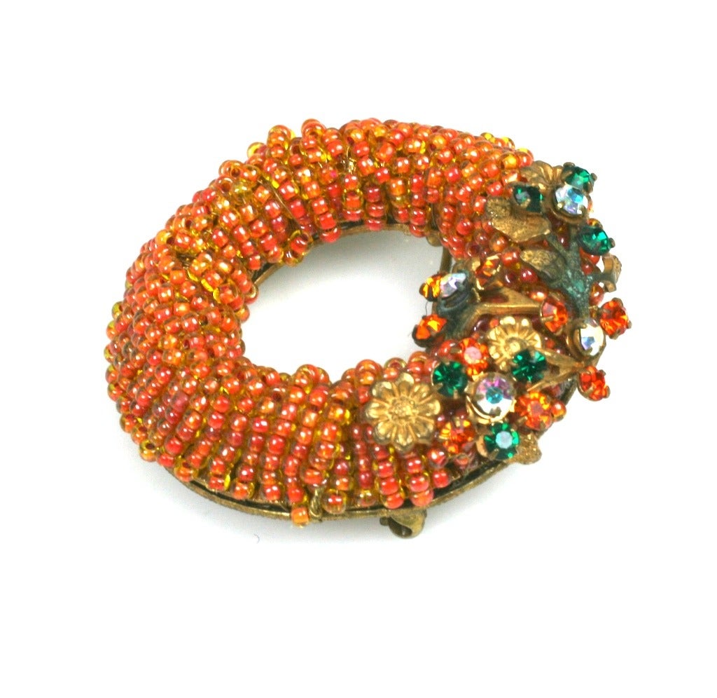 Orange Seed Bead Wreath Brooch probably made by Robert, NY in the 1950's. 
Orange lined yellow seed beads are wrapped tightly around a circular base and topped with filigree findings with colored pastes in orange, aurora and emerald.
2