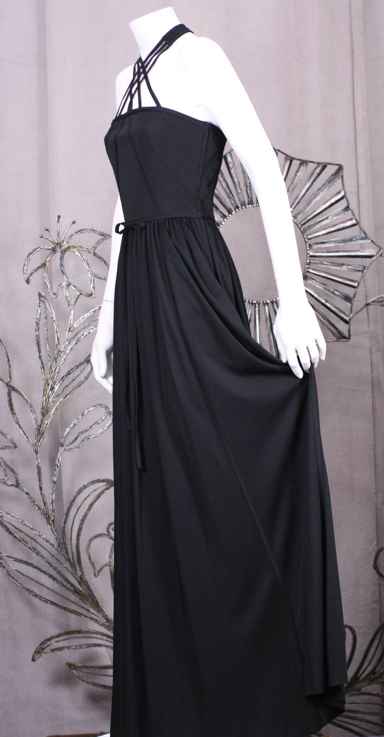 Donald Brook's one piece synthetic black jersey gown with interlaced halter straps which continue down bodice and skirt of gown. Fully gathered skirt with self fabric belt with side zip entry.
Buttons at back of neck with 3 covered buttons. Size: