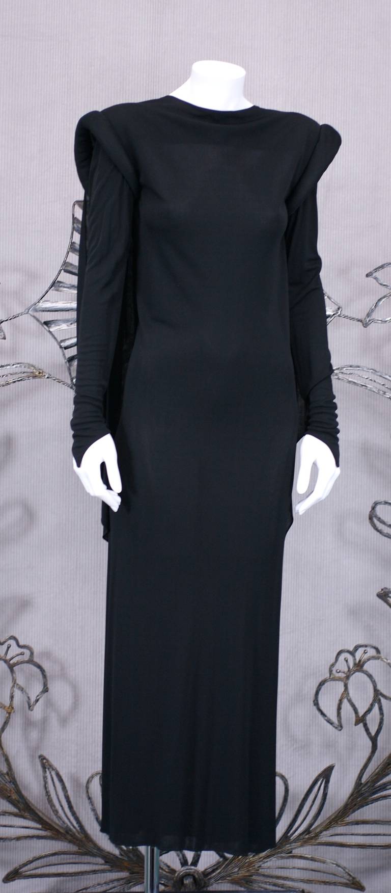 Marie Pierre Tattarachi's black matte jersey gown with dramatic back interest. Large padded roll shoulders, a vestige of the precedent disco period anchors the clean, long lines of the gown.
A massive draped cowl falls from the shoulders on the
