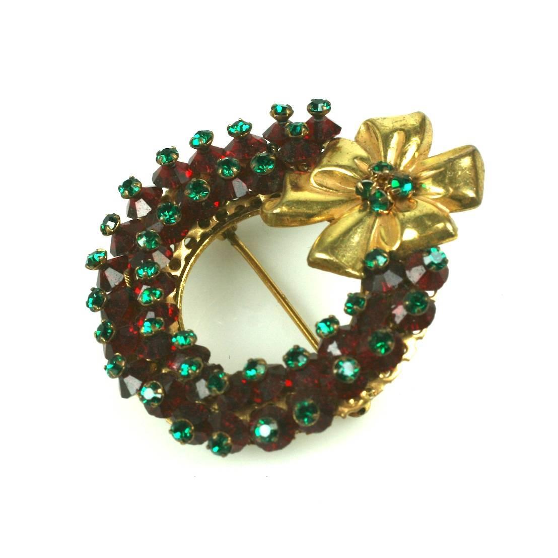 Miriam Haskell's rare Holiday Christmas Wreath Brooch. The circular wreath and applied focal holiday bow are hand sewn with deep red Swarovski faceted crystals and emerald green rose monte crystals. Set in signature Russian gilt filigree. 1950's