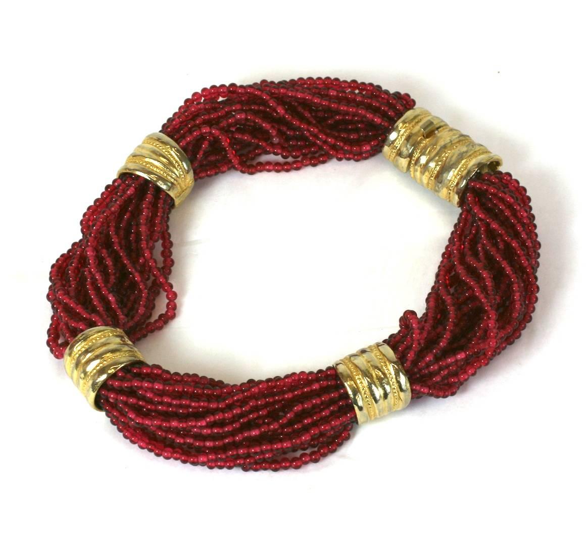 Audace collana a torsione realizzata con fili multipli di perline in pate de verre color rubino, trattenuti da distanziatori tubolari dorati. Anni '80, USA. Condizioni eccellenti.  18