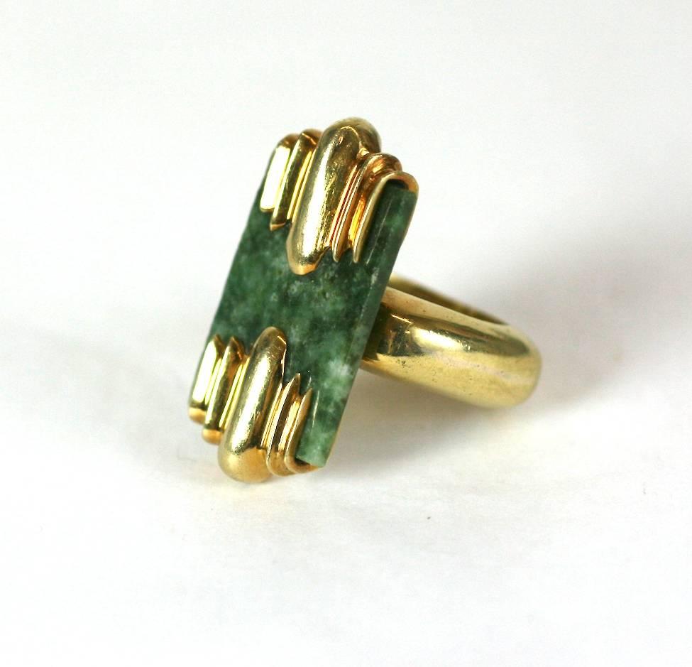 Modernistischer Ring aus Jade und 18 Karat Gold mit Art-Déco-Anklängen.  Die gesprenkelte Nephrit-Jade-Plakette wird von zwei großen gerippten Deco-Platten gehalten, die über einem schweren, abgerundeten, aber abgewinkelten Ringschaft hängen.
Eine