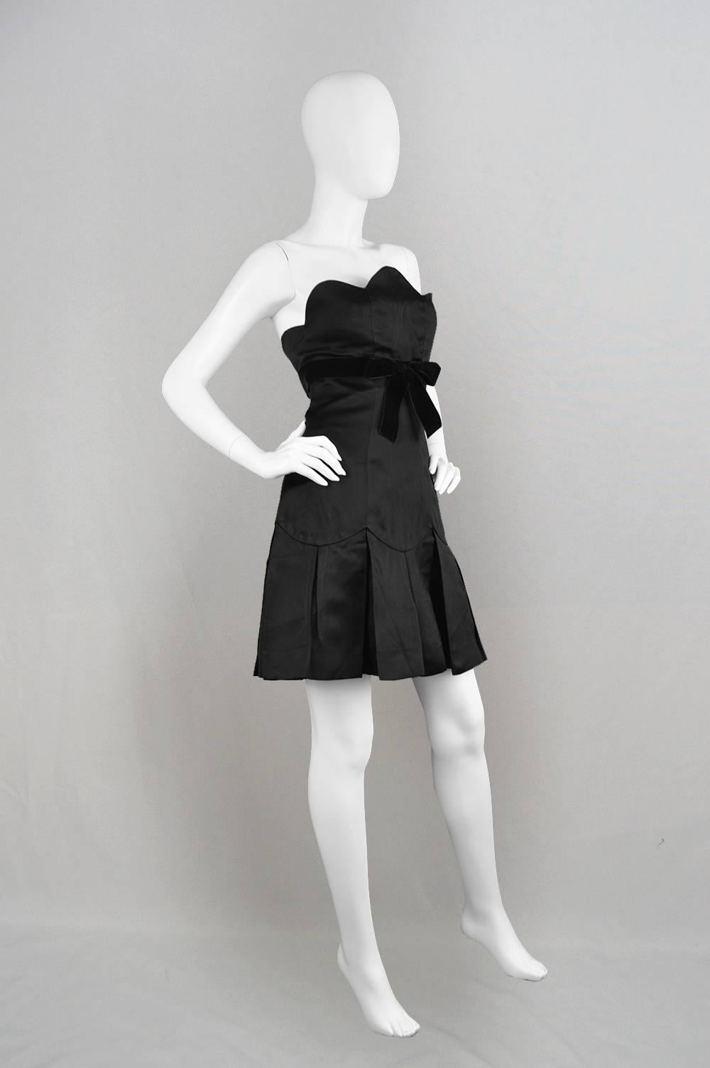 A chic and sophisticated vintage Chanel boutique party dress with lots of sex appeal. In a thick black silk with a scalloped bust that highlights the decolletage and a velvet bow that highlights the empire waist. The skirt is pleated and has a tulle