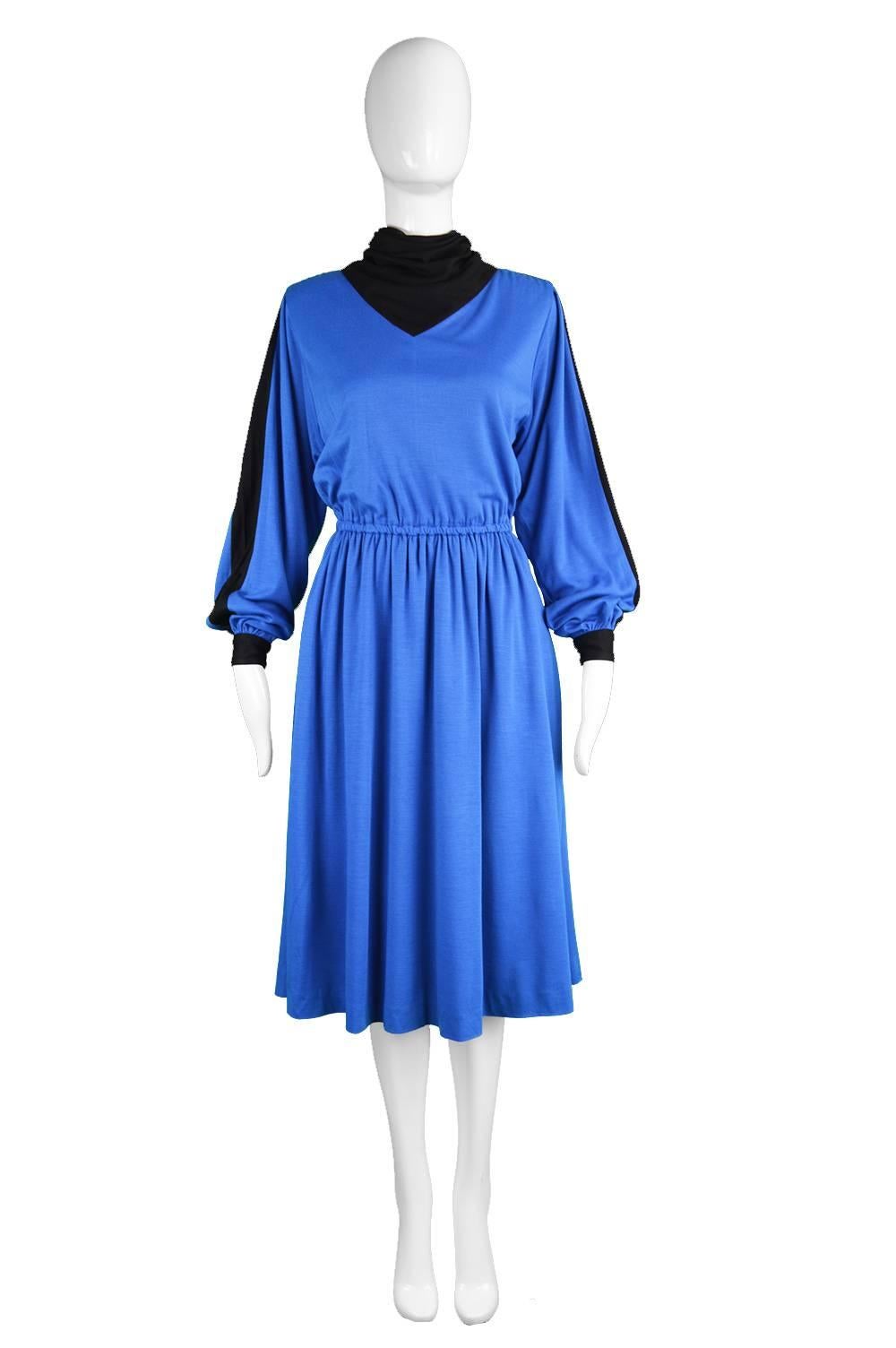 A chic vintage dress from the early 80s by luxury Swiss label, Akris. In a blue wool blend fabric with a black cowl neck and stripes down each sleeve. The top is voluminous for a casual look with an elasticated waist that creates a flattering